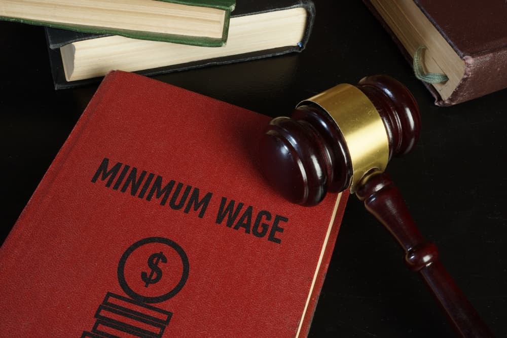 Minimum wage increase and minimum wage law are shown using a text on the book and photo of gavel