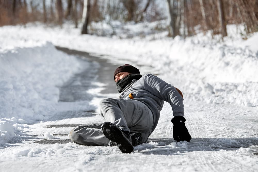 An injured man lying on the road after an accident caused by black ice during the winter season, reflecting a dangerous downfall.