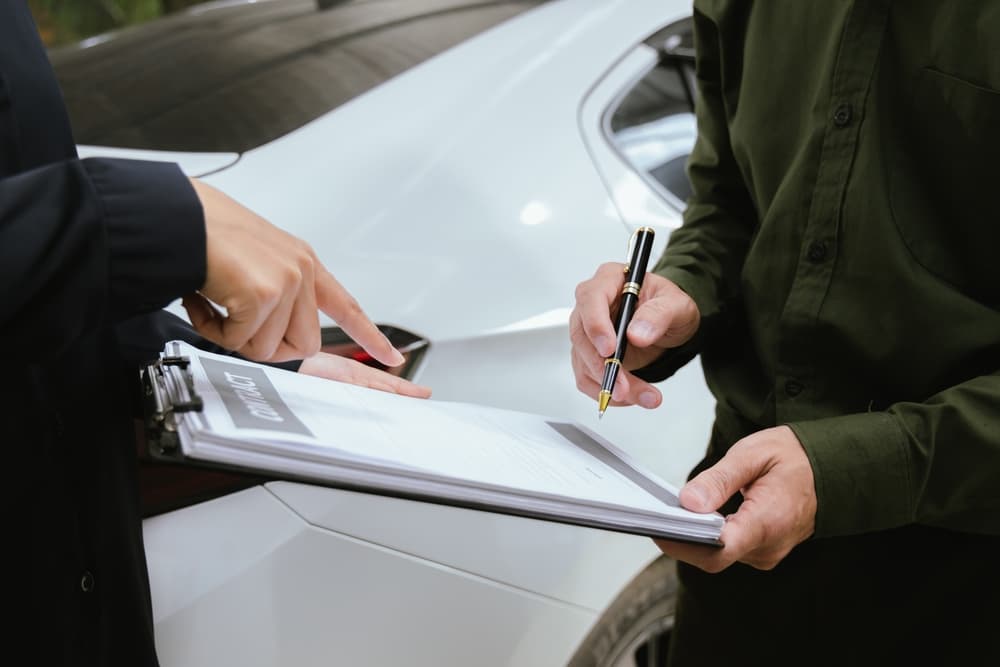 An insurance agent reviews a car accident claim with a customer, holding a clipboard as they discuss financial arrangements for vehicle damage and settlement.